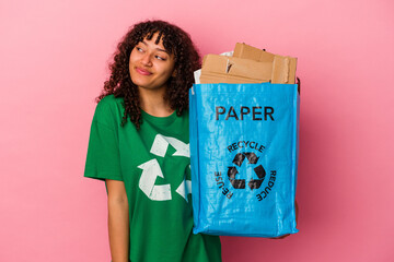 Poster - Young caucasian woman holding a recycled plastic isolated on pink background dreaming of achieving goals and purposes