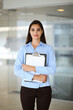 © volha_r - A friendly young businesswoman or female student is standing with some papers in the office. Lifestyle and diverse people concept