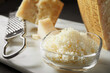 Parmigiano in pieces and grated. Glass bowl with grated Parmesan cheese and grater on marble cutting board. Closeup, selective focus.