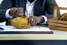 African Businessmen Inspect The Quality By Cutting Through The Inside Of The Cocoa Pod With A Knife On His Desk
