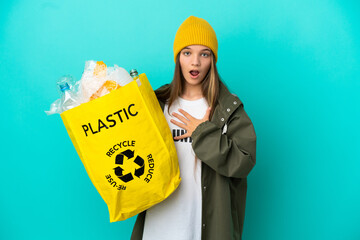 Wall Mural - Little girl holding a bag full of plastic bottles to recycle over isolated blue background surprised and shocked while looking right