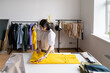 Concentrated self employed female dressmaker work on new clothes collection with pattern of bright yellow raincoat on sewing table in tailoring studio. Young girl dressmaker busy with work in workshop