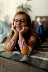 Wall Mural - Close up photo of cute smiling little girl, laying on stomach at couch, chilling and relaxing.