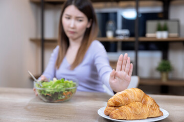 Wall Mural - Asian woman refuses to eat her favorite bread and opts for a healthy salad.