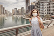 © EdNurg - Frowning woman wearing a medical mask walks down a street in Dubai's Marina district during covid corona virus pandemic outbreak
