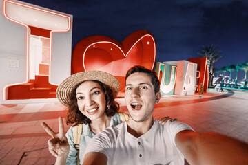 Wall Mural - Happy couple tourists taking selfie photos and enjoys their journey near the caption I love UAE at night. Sightseeing attractions in Dubai