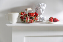 White Metal Basket With Wooden Handle With Fresh Strawberries, Corrugated Ceramic Cup Of Tea, Plaster Apollo Head On A Beige Table. Still Life.