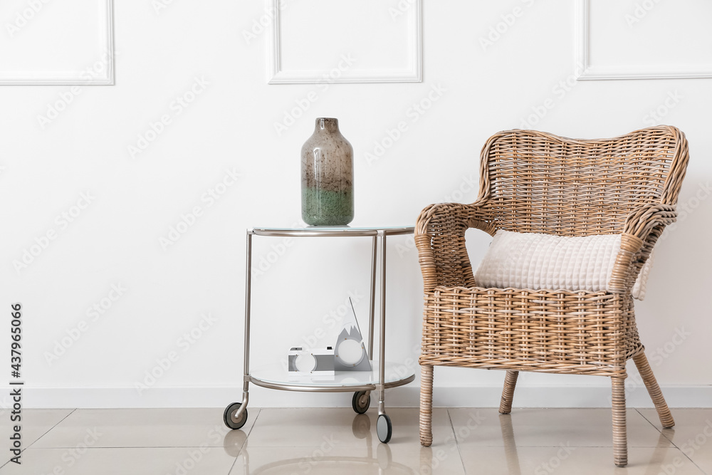 Wicker armchair and table with decor near light wall