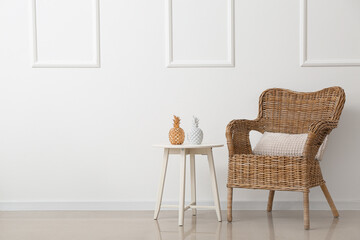 Wicker armchair and table with decor near light wall