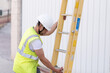 © CHESTER - telecommunications technician with safety helmet and reflective vest, deploying a yellow ladder while looking down.