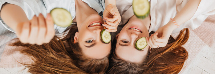 Wall Mural - two girls make homemade face and hair beauty masks. cucumbers for the freshness of the skin around t