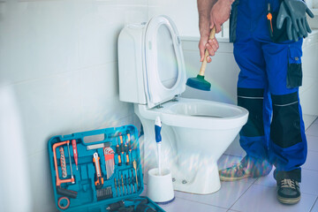 Wall Mural - Professional plumber in uniform is repairing toilet bowl in the domestic bathroom with the help of tools