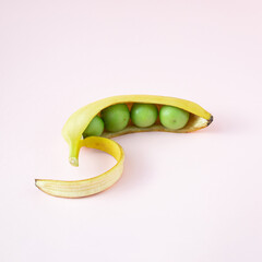 Wall Mural - green tomato in the peel of a yellow banana on a pink background. Minimal layout