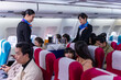 Two young beautiful Asian flight attendant serving food and drink to passengers on airplane. Two stewardess pushing food cart along aisle to serve the customer. Airline service business concept.