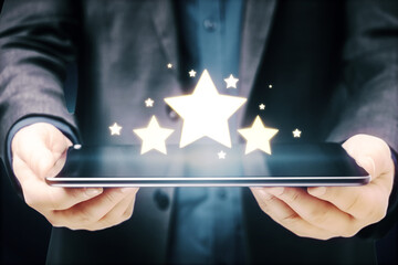 Businessman hands holding tablet with glowing stars on blue background. Customer feedback and online ranking concept.