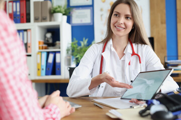 Woman doctor showing information to patient on digital tablet in clinic