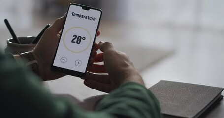 man is controlling system of smart home using app in cellphone, adjusting temperature in room and switching on security system, closeup view
