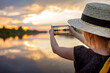 © Maria - Pretty preteen girl in summer straw hat taking selfie for cellphone at beautiful sunset on lake, lifestyle, local travel concept, young blogger