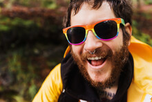 Gay Man, With Beard, Piercings And Tattoos Laughing Looking At Camera Wearing Rainbow Pride Sunglasses.