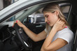 Young woman suffering from neck whiplash, sitting in drivers seat of her car