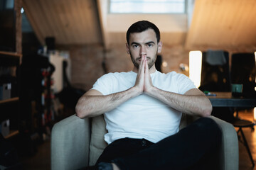 Portrait of handsome young brunette man in white t-shirt sitting in armchair at home