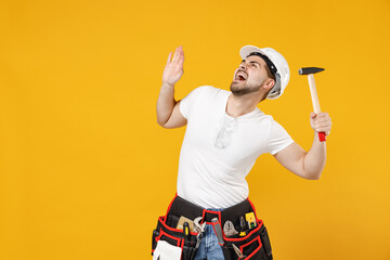 Young scared frightened employee handyman man 20s in protective helmet hardhat glasses hold hammer isolated on yellow background Instruments accessories renovation apartment room Repair home concept.