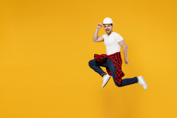 Full length side view young employee handyman man 20s wearing protective helmet jump high run isolated on yellow background. Instruments accessories for renovation apartment room. Repair home concept.