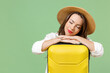 Close up tired traveler tourist woman in casual clothes hat leaning on yellow suitcase valise sleep isolated on green background Passenger travel abroad weekends getaway Air flight journey concept