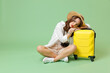 © ViDi Studio - Full length sad tired troubled traveler tourist woman in casual clothes hat leaning on suitcase sitting isolated on green background Passenger travel abroad weekend getaway Air flight journey concept.