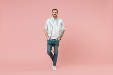 Full length young happy cheerful friendly caucasian unshaven man 20s in blue striped shirt white t-shirt look camera isolated on pastel pink color background studio portrait. People lifestyle concept.