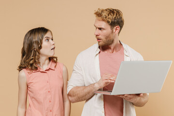 Young confused parent man with child teen girl in casual clothes. Daddy little kid daughter using laptop pc computer look to each other isolated on beige background. Father's Day Love family concept.