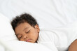 © ronnachaipark - black african american baby sleeping on a white mattress.