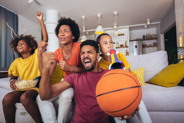 Happy African American family watching tv and cheering basketball games on sofa at home.