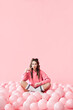 © GVS - Young thoughtful woman sitting on floor with pink balloons on pink pastel background