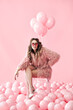 © GVS - Confident fashion woman sitting on chair posing on many pink balloons background