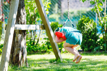 Wall Mural - Happy little preschool girl having fun on swing in domestic garden. Healthy toddler child swinging on sunny summer day. Children activity outdoor, active smiling kid laughing