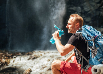 Wall Mural - man with backpack dressed in active trekking clothes drinking the water from touristic flask sitting