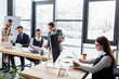 © LIGHTFIELD STUDIOS - Businesswoman holding papers near coffee, computer and multiethnic colleagues in office