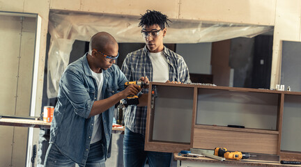 Two young black man carpenters assembling furniture part in the workshop.	