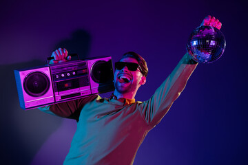 Poster - Photo of cheerful young cool happy man hold hand boombox disco ball clubber isolated on neon background