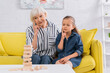 © LIGHTFIELD STUDIOS - Pensive kid looking at blurred blocks wood tower game near grandmother