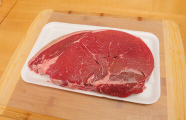 Raw uncooked sirloin steak in a butcher tray on a wooden cutting board.