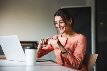 Beautiful Caucasian business woman having conversation online with friends and showing gesture heart in the cabinet