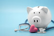 © Nudphon - Piggy bank with stethoscope and heart isolated on light blue background with copy space. Health care financial checkup or saving for medical insurance costs concept.