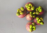 Bunch of isolated organic farm fresh purple fruit mangosteen also known as garcinia mangostana and mangostan stacked on wet white background with water drops and copy space. Fruits close up top view.