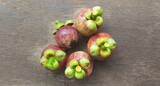 Bunch of isolated organic farm fresh purple fruit mangosteen also known as garcinia mangostana and mangostan stacked on wooden background with water drops and copy space. Fruits close up top view.