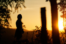 A Girl In Silhouette In Sun Set In The Forest. Summer Days. It Is Hot And Warm. Two Sisters Are Playing In The Woods. Golden Hour With Strong And Bright Sunlight.
