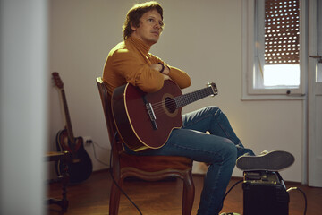 Wall Mural - Male musician playing acoustic guitar on the amplifier in retro vintage room.