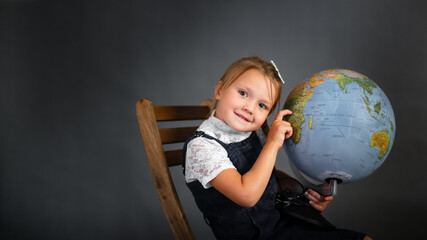 Wall Mural - Girl child schoolgirl in school uniform with globe, classic school photos, dark background