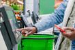 The finger of an African man in close-up at the supermarket checkout selects the desired product on the electronic screen of the cash register with a phone in his hands against the background of green
